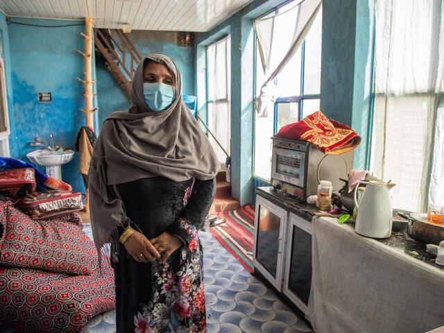 Noor stands in a sunny kitchen with blue walls. 