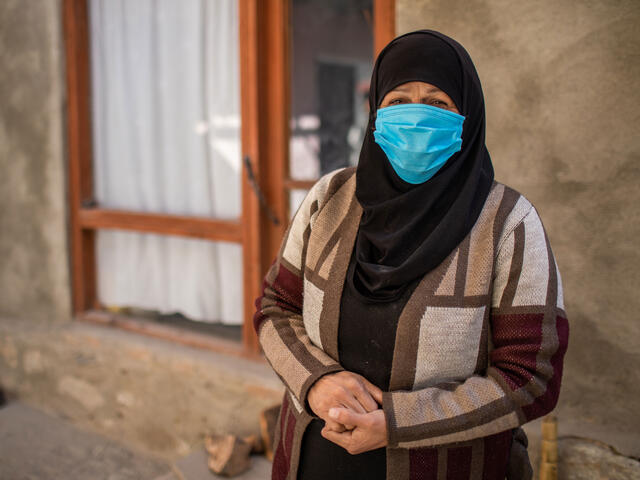 Wearing a mask, Zulaykha stands in front of a building and looks at the camera