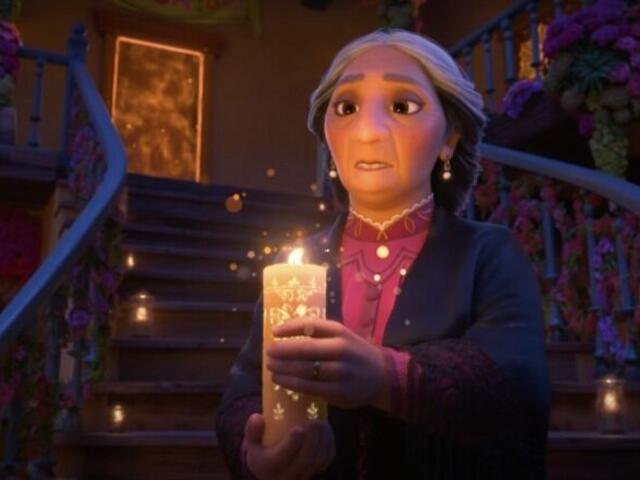 Abuela Alma walks in a darkened hall holding a candle 