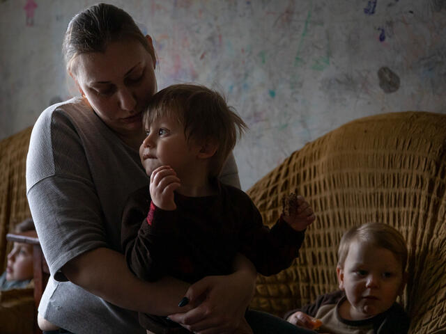 A mother sits holding one of her sons on her lap. Two other children sit in chairs behind them. 