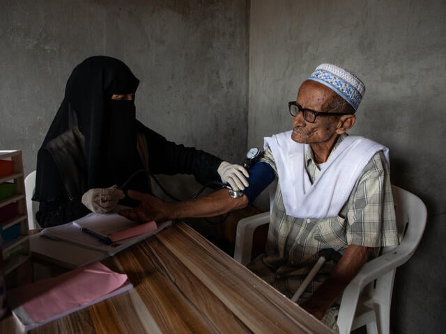 A female IRC health worker measures the blood pressure of an elderly man in Yemen.