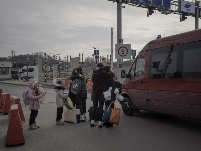 Refugees from Ukraine embrace while standing next to a van in Poland. 