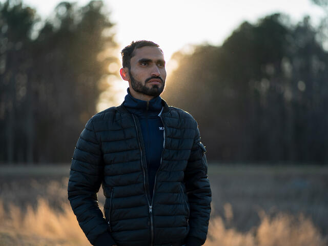 Photojournalist Mohammad Anwar Danishyar stands in front of a forest in the evening. 