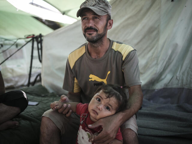 Father sits with his daughter outside their family tent in the Alexandria refugee camp