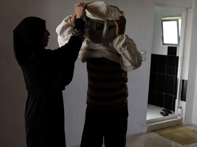Syrian woman helps her husband put on his protective beekeeping suit