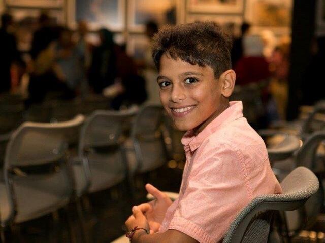Syrian boy sitting in chair, smiling, at a UN Refugee Event in Los Angeles