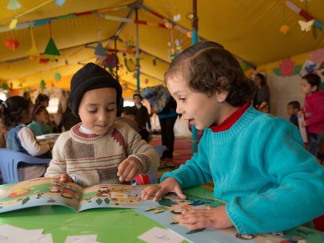 Two Syrian children read books in a tented classroom