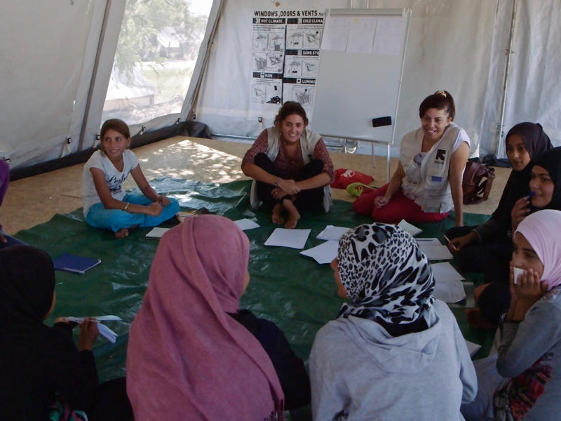 Girls sit in a circle playing a game in a tent that serves as an IRC "safe space" in a refugee camp in Greece.