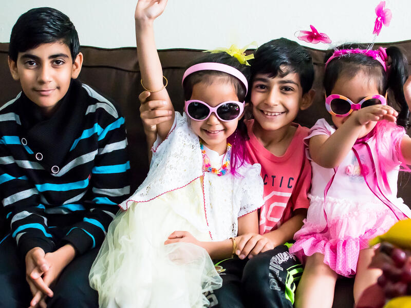 Syrian refgees Ahmed, Ruha, Rahaf, and Bader arrived with their parents and two older siblings in San Diego in November 2016. Syrian children resettled in San Diego pose for a silly photo on their couch while playing dress-up.