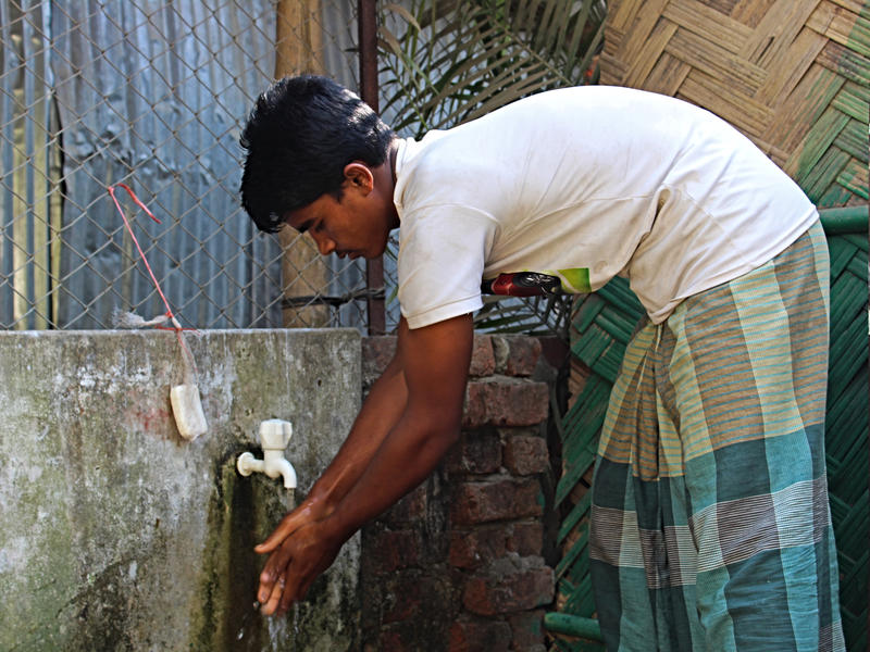 A young refugee washes his hands under an outdoor tap in the Cox's Bazar refugee camp, where the International Rescue Committee assists Rohingya refugees. A young refugee bends over to wash his hands under an outdoor tap in the Cox's Bazar refugee camp.