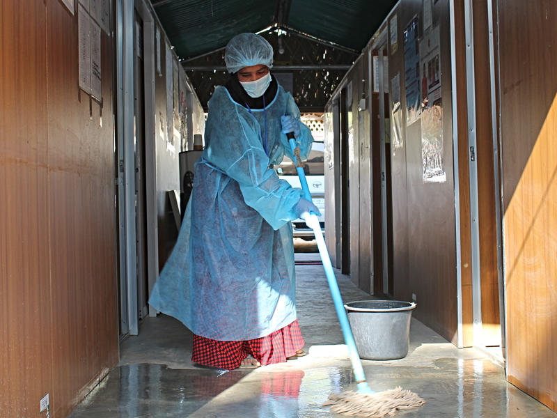 A health worker mops the floors as she disinfects an IRC 24-hour health facility in Cox's Bazar refugee camp