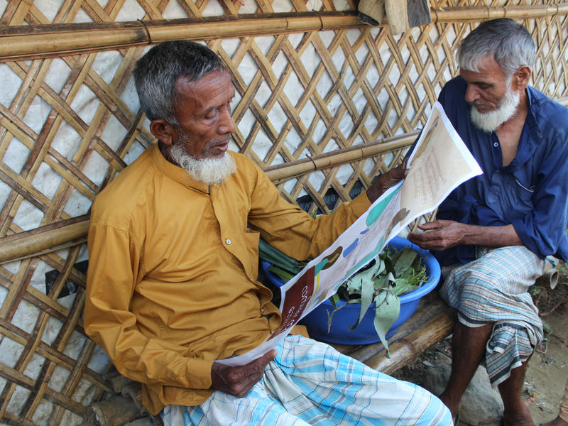 Two elderly men sit reading coronavirus information from the IRC in the Cox's Bazar refugee camp