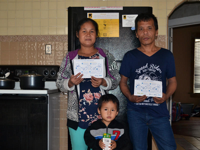 The Htoo Family received in-home education about energy efficiency by the IRC in Salt Lake City. The Htoo Family standing in their home with energy efficiency signs.