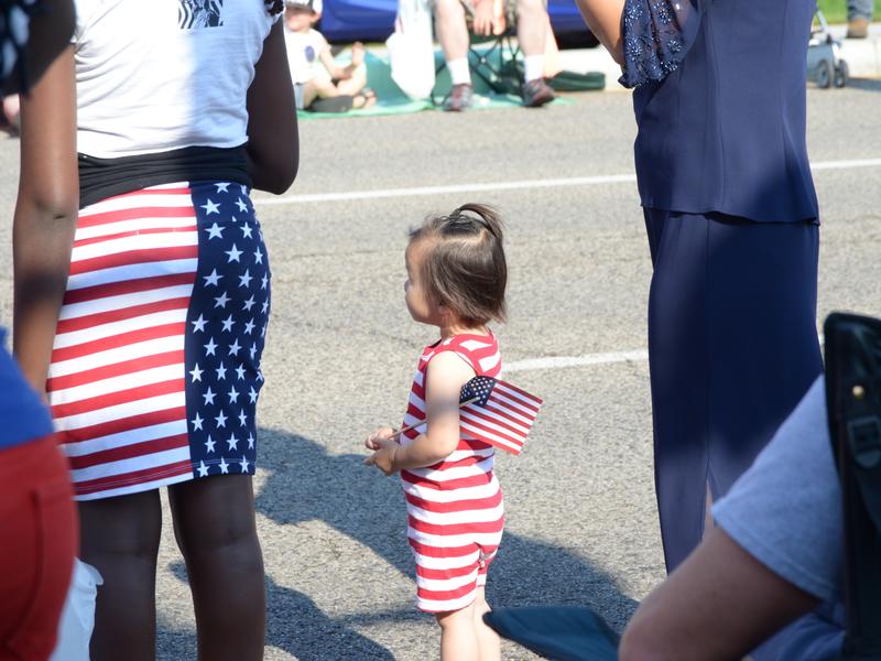 Joanne's brought a family from the D.R. Congo to a parade Toddler watching fourth of July parade with United States flag in hand.