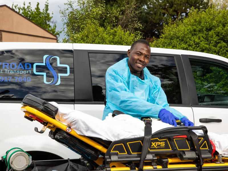 Jonathan Amissa working at his medical transportation business Jonathan Amissa, wearing scrubs, stands in front of a van with his hands on a stretcher. The van has a logo for Skyroad Medical Transport, his medical transportation business.