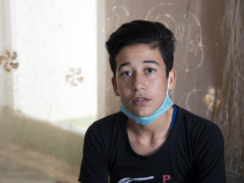 Fifteen-year-old Muhammad, wearing a mask around his chin, sits and looks at the camera. 