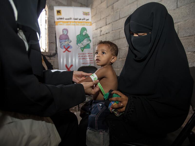 An IRC health worker in Yemen measures a toddler's upper arm for signs of malnutrition as he sits on his mother's lap.