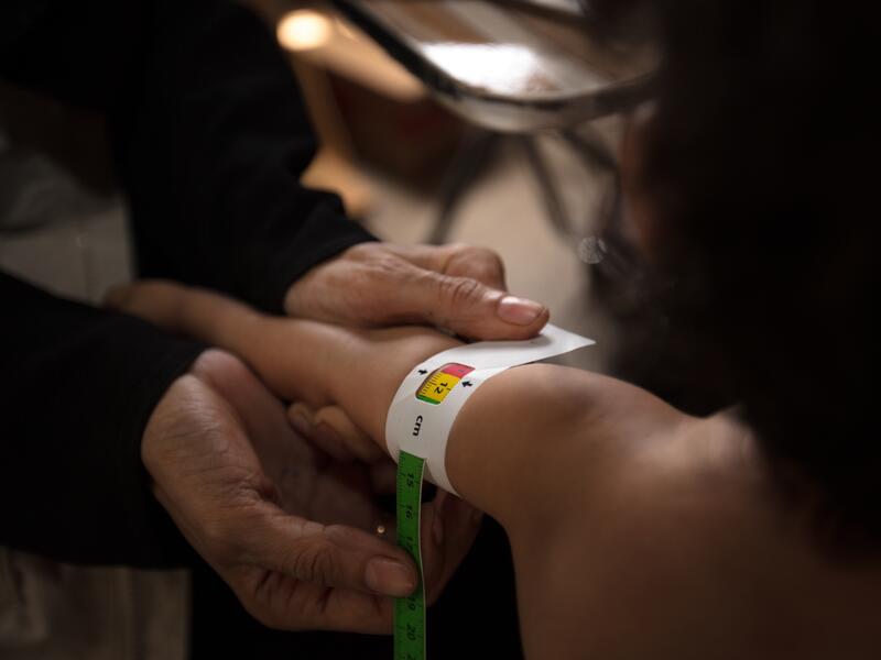 An IRC health worker measures a child's upper arm with MUAC tape to check for signs of acute malnutrition.