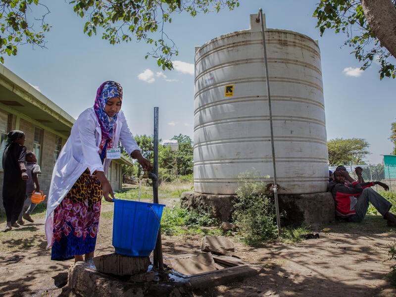 An IRC health worker in Ethiopia collects water in a large bucket  
