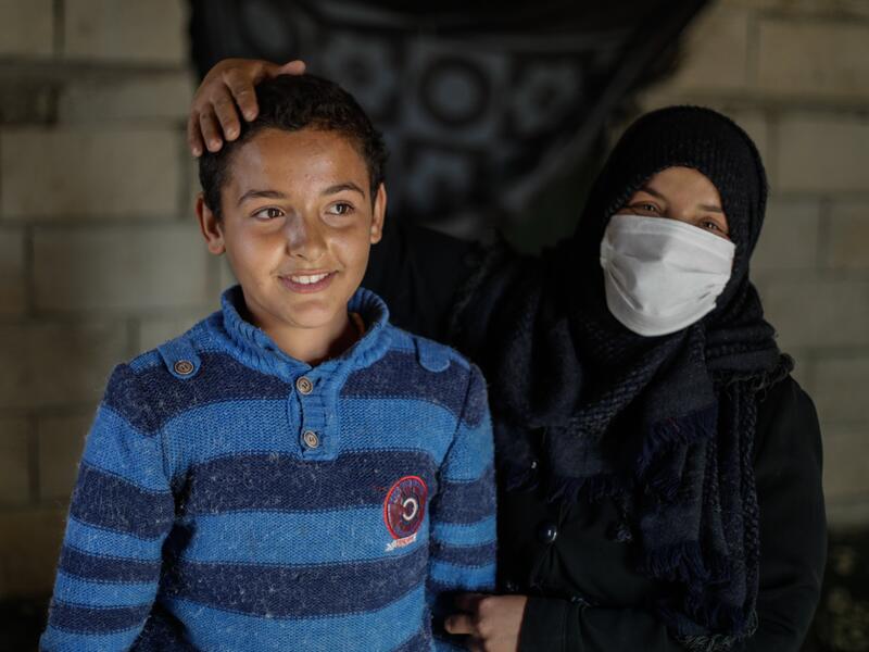 Tareq with his mother, Muna Tareq and his mother, Muna, in their home. She is holding his arm and has her hand affectionately resting on his head.