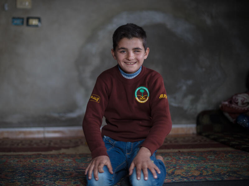 Ali in his home Smiling, Ali sits on a rug on the floor of his home.