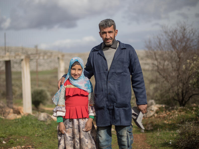 Sara and her father, Emad, stand outside. He has his arm around her and they are both looking at the camera. 