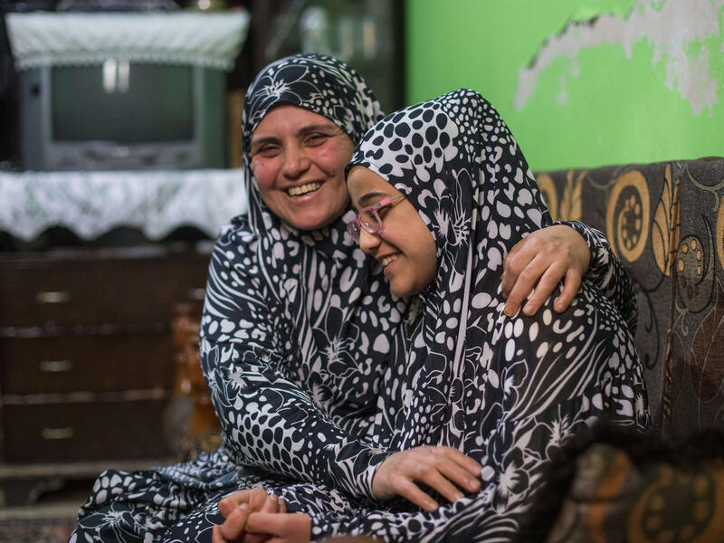 Salam and her mother, wearing matching outfits, sit in a couch and laugh together. 
