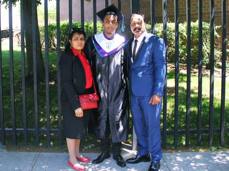 Sarujen and his parents, Shanthini and Sivakumar, at his high school graduation. Wearing a graduation cap and gown, Sarujen stands in front of a fence with his parents on either side of him.