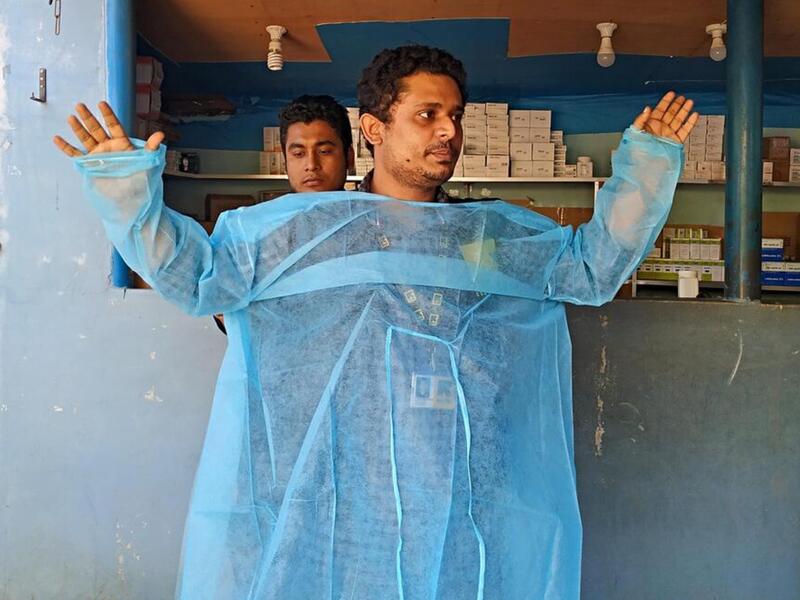 Dr, Mahmudul Hossain stands in front of a group of health care workers and volunteers and demonstrates how to correctly put on a medical gown. 