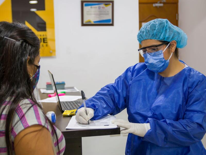 Dr. Gomez with a patient In full PPE, Dr. Gomez writes on a chart while standing at a desk while speaking to a patient.