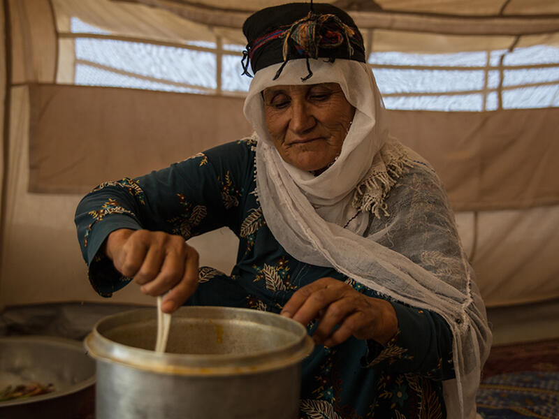 An Afghan woman stirs food in a pot while sitting in a tent in a refugee camp 