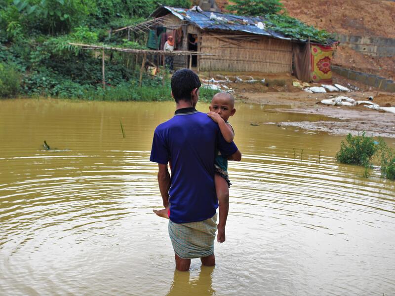 Rohingya refugee Nurul Hauqe, 50, and his family moved to the Cox's Bazar refugee settlement in Bangladesh after escaping ethnic violence in Myanmar's Rakhine state. Refugees living in the crowded camp have been beset by natural disasters, including monso Nurul Hauqe, 50, carrying his two-year-old son, wades through nearly knee-high monsoon floodwater in Cox's Bazar, Bangladesh after escaping violnmar.ence in Mya