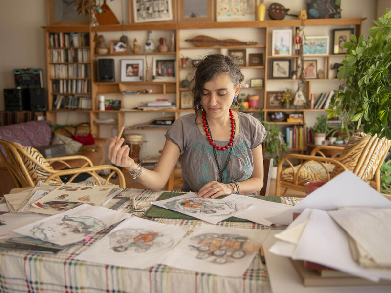 Diala, sitting at her desk holding a pencil, reviews preliminary sketches of her "Refugees are courageous" illustration.
