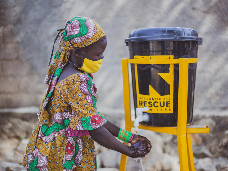 Children at IRC safe spaces are encouraged to wear masks, distance, and properly wash their hands. 10-year old Anastasie, wearing a face mask to protect her against COVID-19 washes her hands at an IRC wash stand fashioned from a covered plastic bucket.