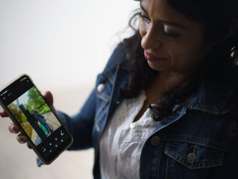 Wearing a jean jacket, Rosa holds out her iPhone. There is a picture of her daughter on the screen. 