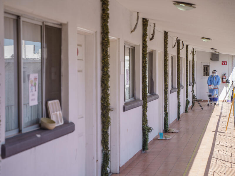 The IRC and International Organization of Migration-supported triage hotel that Rosa manages. A health care worker in full PPE pushes a cart down an outdoor walkway in front of doors to hotel rooms.
