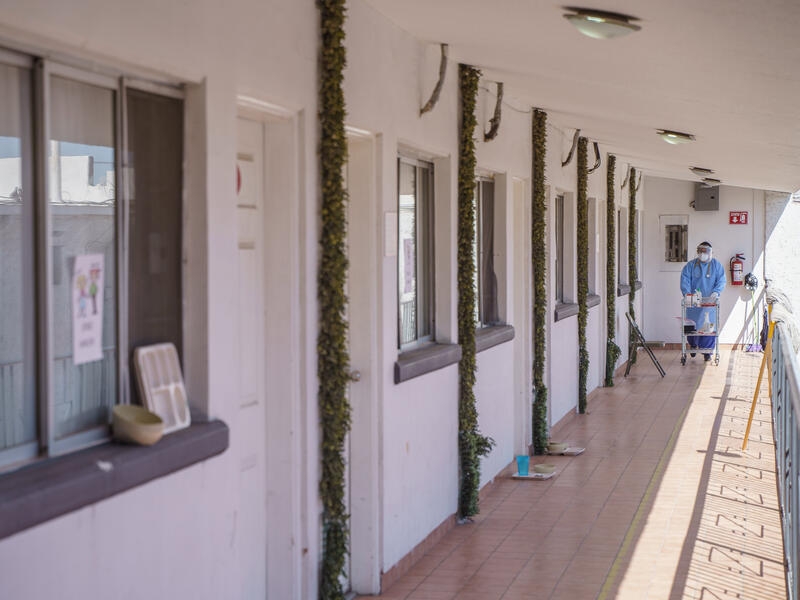Un "hotel filtro" apoyado por el Comité Internacional de Rescate y la Organización Internacional para las Migraciones. Un trabajador de la salud con EPP completo empuja un carrito por las habitaciones de hotel.