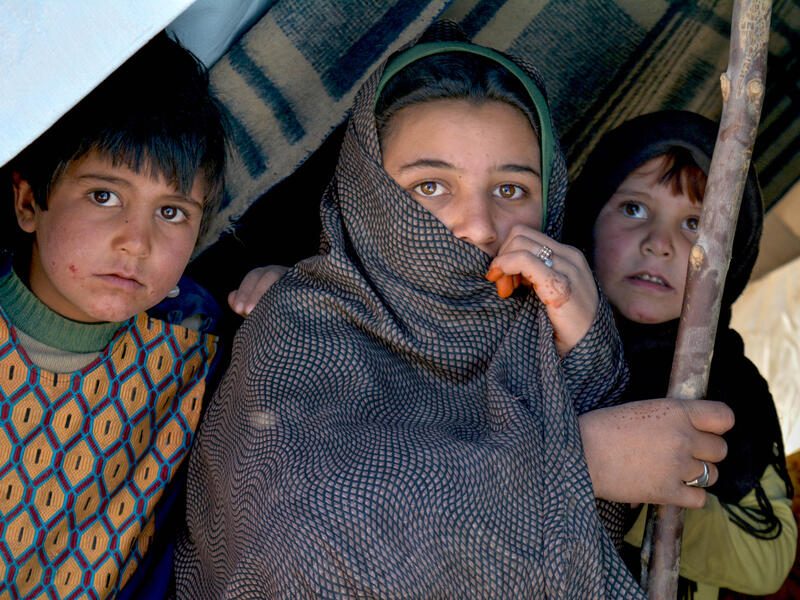 An adolescent girl and two young children look out anixiously from a tent in a camp for displaced Afghan families.