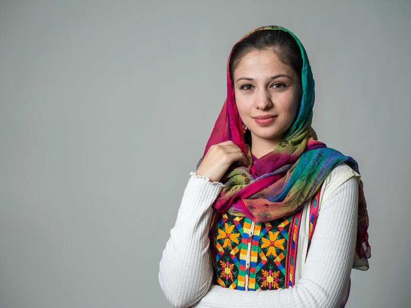 Muska Haseeb, who fled Afghanistan when she was 12 years old and now lives in Phoenix A portrait of Muska Haseeb on a grey background. She is a young woman in her early 20s wearing brightly colored clothes.