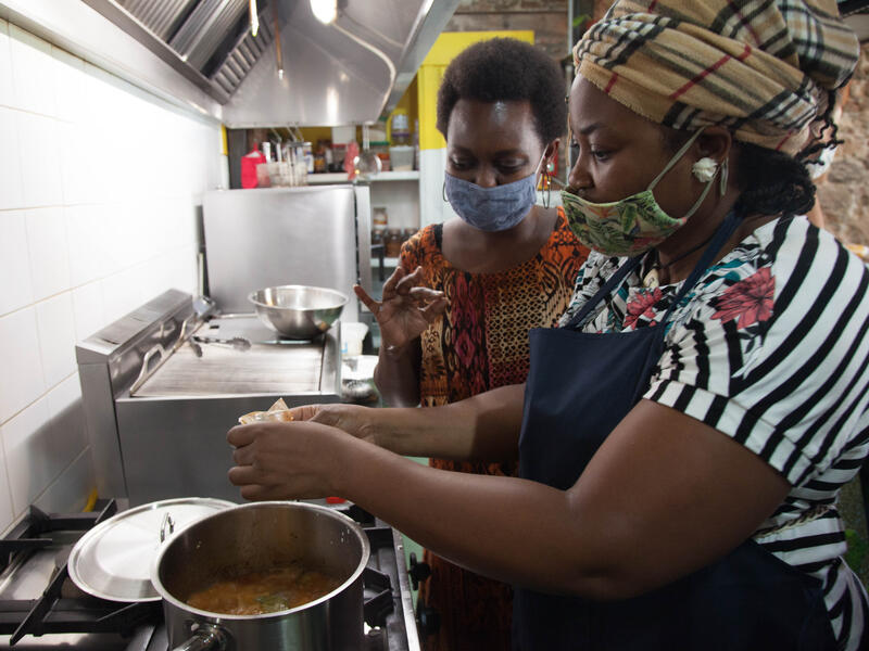 Koteu and Sandra cooking together. Two women wearing masked cook together over a stove.