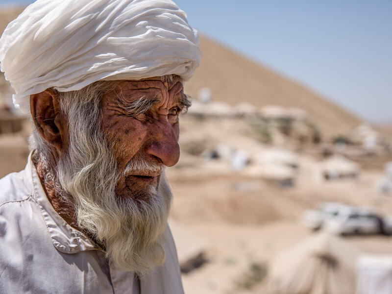 A 67-year-old Afghan man stands overlooking the tent camp where he and his wife live after being displaced by drought.
