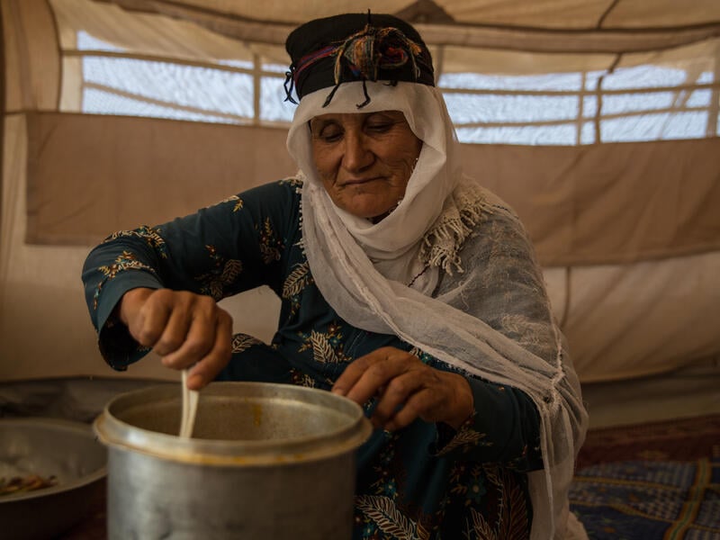 An elderly Afghan woman sits in her tent stirring a cooking pot in a camp for displaced families in Afghanistan.