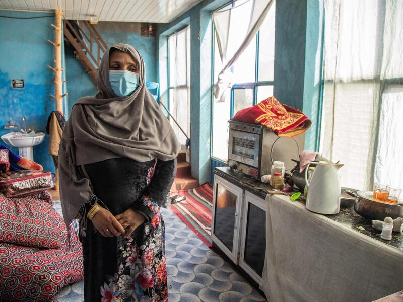 Noor, a mother of three, stands in the kitchen of her aunt, where she is staying after having to flee her home Noor stands in a sunny kitchen with blue walls.