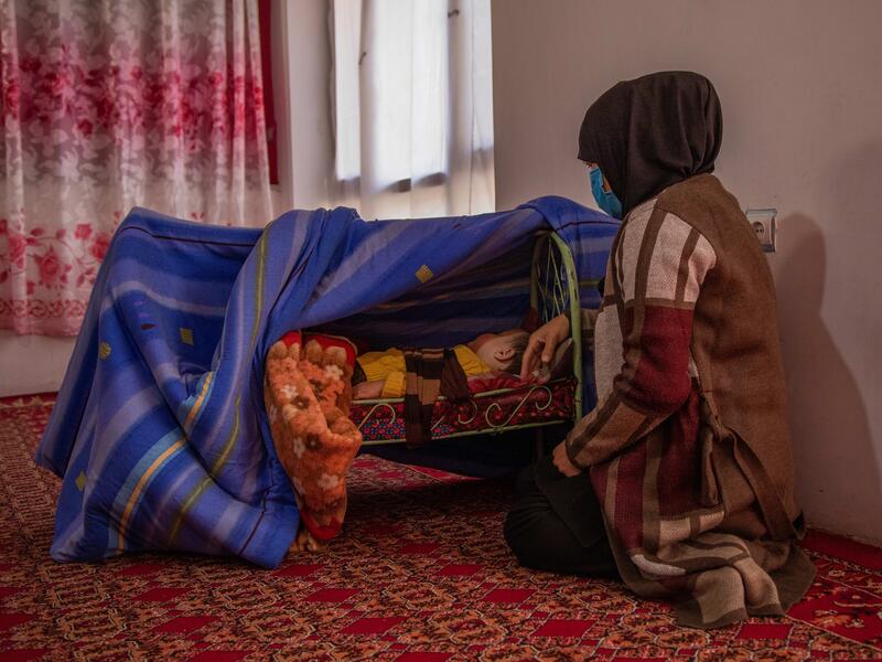 Zulaykha worked in human rights in Afghanistan before fleeing her home with three of her children. Zulaykha kneels on the ground next to her one-year-old son, who is sleeping bassinet on the ground shielded by blankets.
