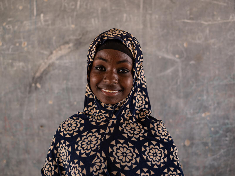 Hauwa, 17, stands smiling by a wall at an IRC safe space for girls in Nigeria