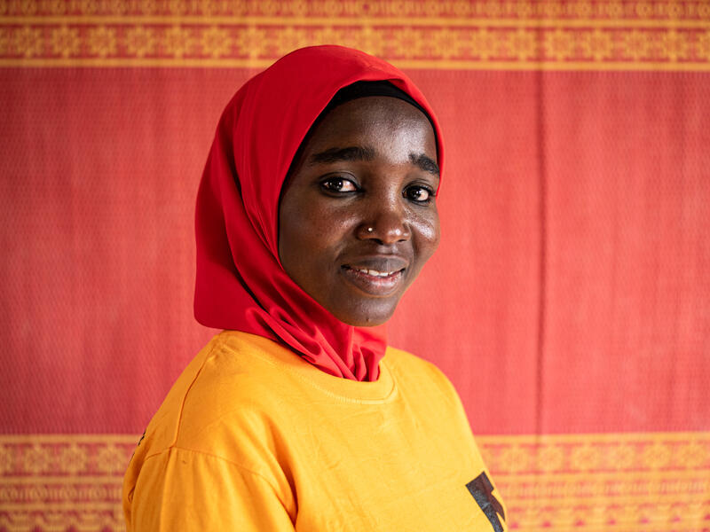 Falmata stands smiling against a brightly colored textile at an IRC safe space for girls in Nigeria.
