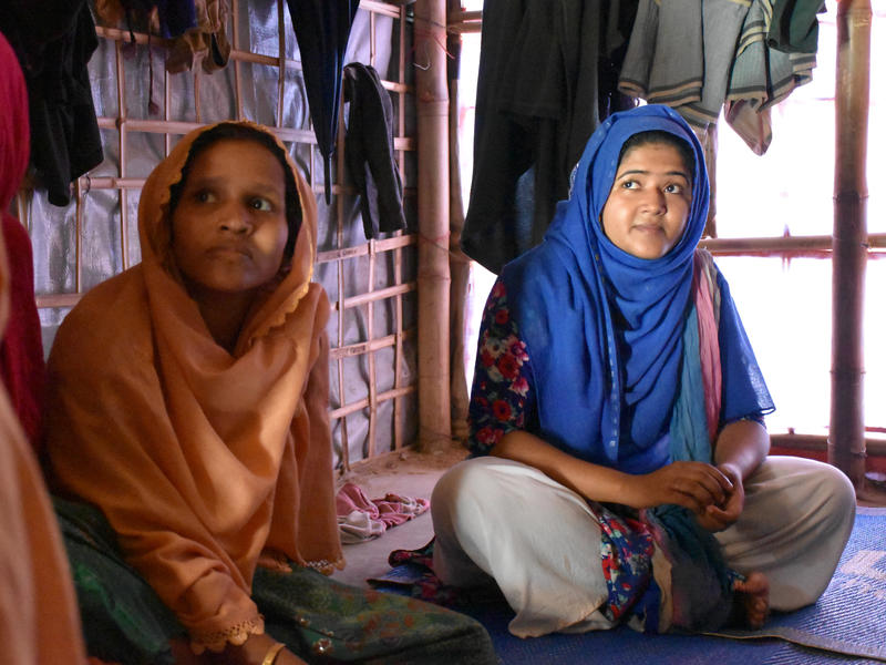 The IRC and our partners are helping refugees get ready for the monsoon, cyclones, and other natural disasters Two Rohingya women sit on mats, listening to an aid worker talk about monsoon preparedness in their refugee camp
