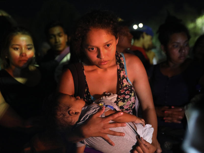 A mother holding a baby waits for a bus with other asylum seekers.