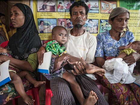 Surrounded by other waiting families, a man holds a young child he has brought to an IRC health center in Myanmar for treatment.