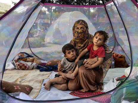 An Afghan woman, 28, who lost her husband in recent fighting sits with her children, ages 5 and 2, in a tent at a makeshift IDP camp in Afghanistan on August 12, 2021. A recently widowed Afghan woman, 28, sits on the floor of a net tent holding holding her two children in a makeshift camp for displaced families in Afghanistan.